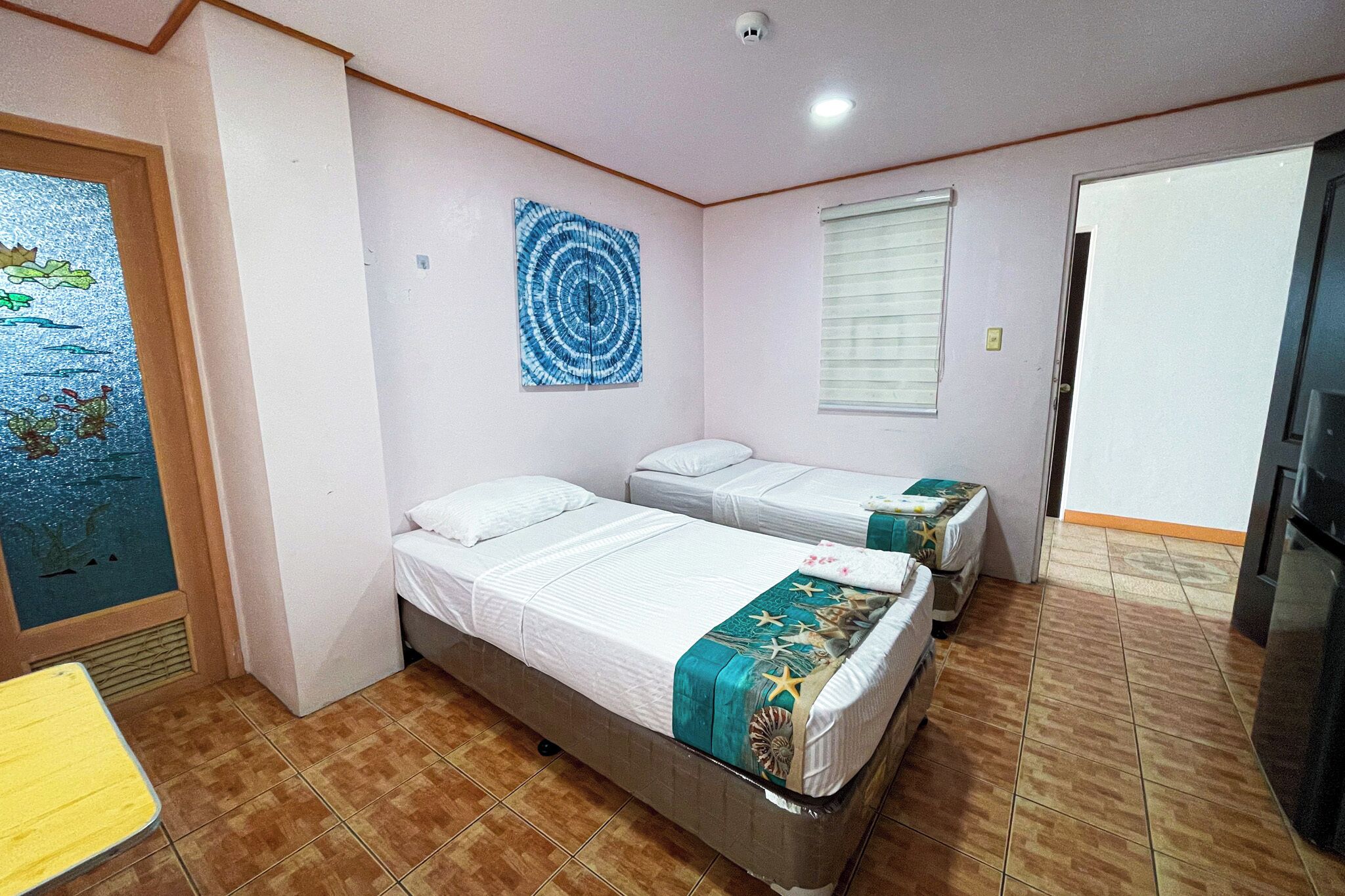 Una habitación con dos camas, un cuadro, una ventana con persianas y una puerta.