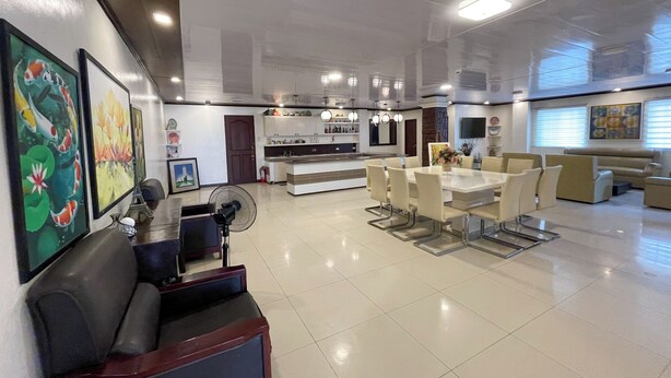 A modern living room with a dining area, a sofa, a fan, and artwork on the walls.