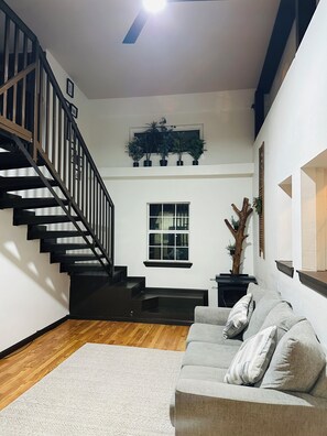Un salon moderne avec un escalier, un canapé, une cheminée et une fenêtre.