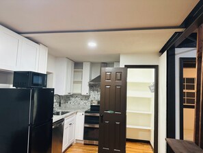 A kitchen with white cabinets, a black refrigerator, a microwave, a stainless steel oven, and a wooden door.
