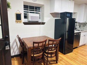 A kitchen with a wooden table, two chairs, a black refrigerator, a microwave, and a window with blinds.