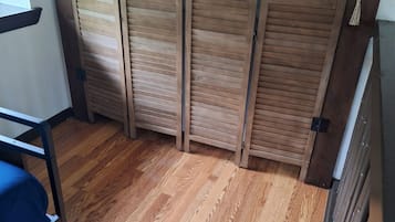 A room with a wooden floor, a bed with a blue mattress, and a wooden partition with decorative cutouts.