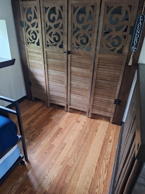 A room with a wooden floor, a bed with a blue mattress, and a wooden partition with decorative cutouts.