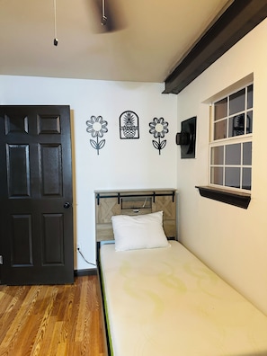 A room with a bed, a wooden headboard, a black door, and wall decorations including a welcome sign and flower designs.