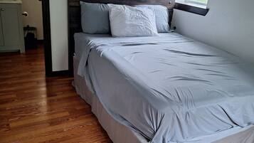 A bedroom with a wooden headboard, a bed with grey bedding, and a window providing natural light.