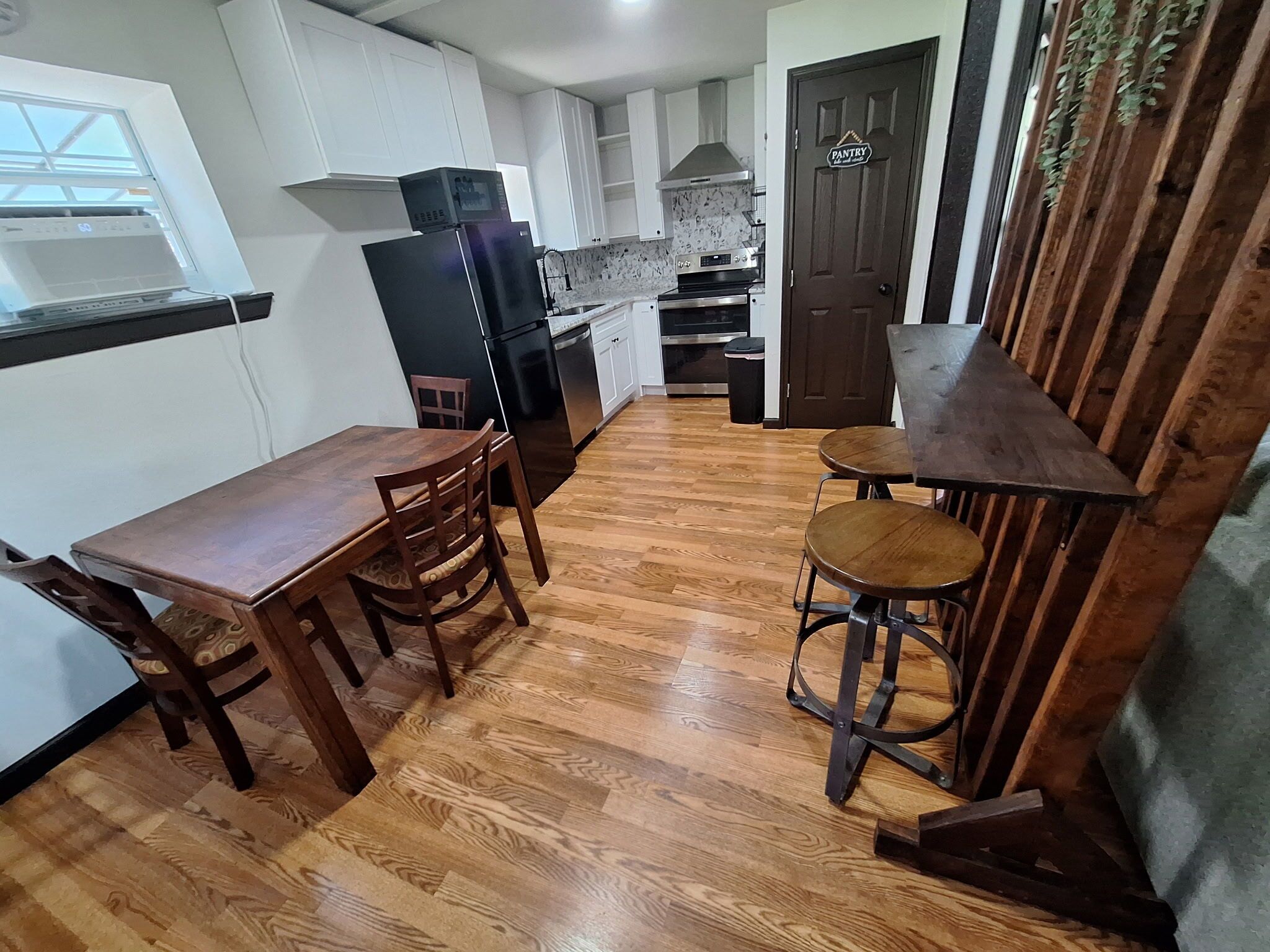 A compact kitchen with a dining table and stools, a refrigerator, oven, and a pantry door.