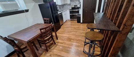 A compact kitchen with a dining table and stools, a refrigerator, oven, and a pantry door.