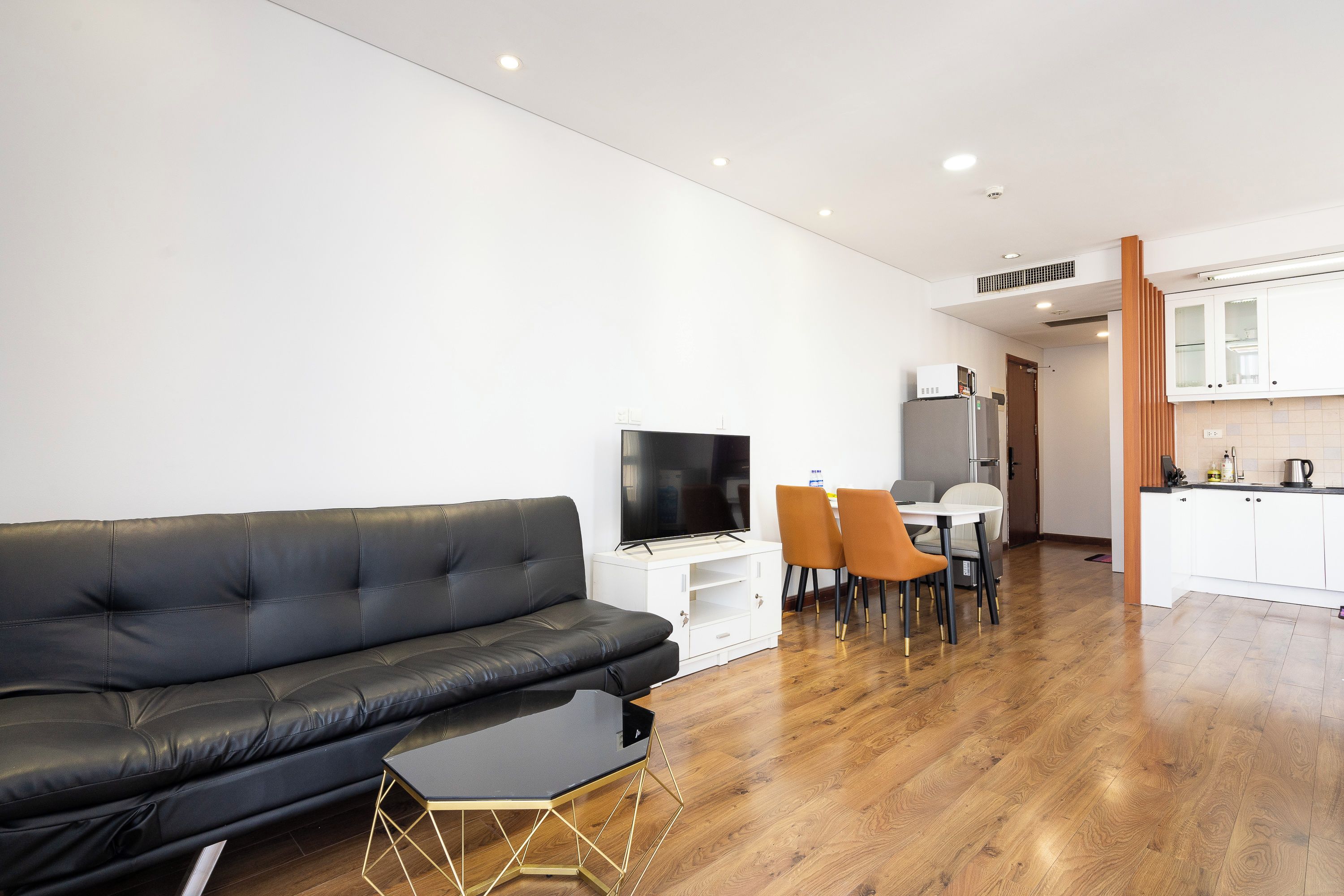 A modern living room with a black leather sofa, a TV, and a dining area with a table and chairs.