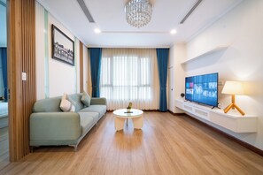 A modern living room with a sofa, a glass coffee table, a TV on a stand, and a chandelier. - IMPERIAL JADE SUITES at LANCASTER (Sai Gon)