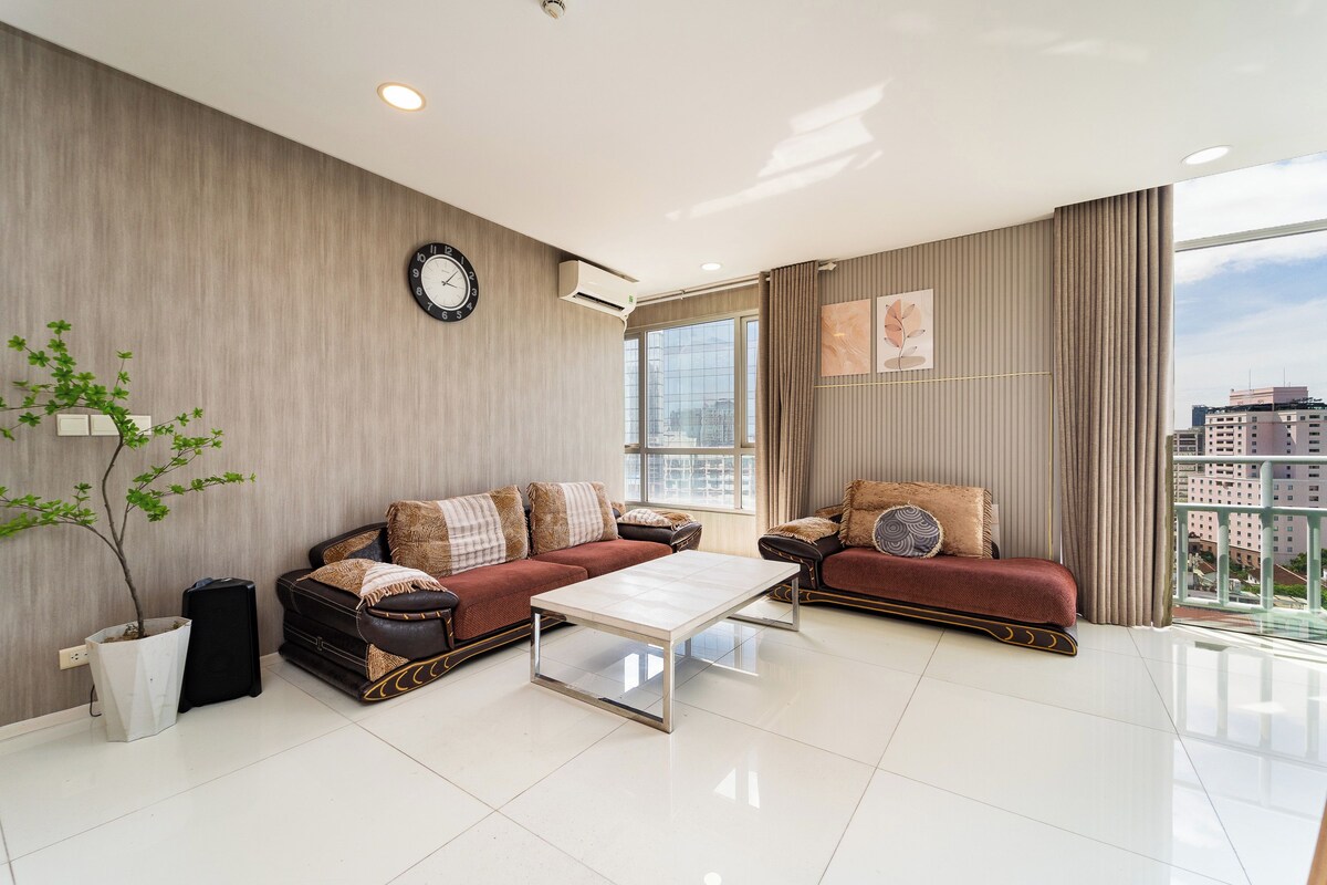 A modern living room with two sofas, a coffee table, a wall clock, and a large window offering a city view.