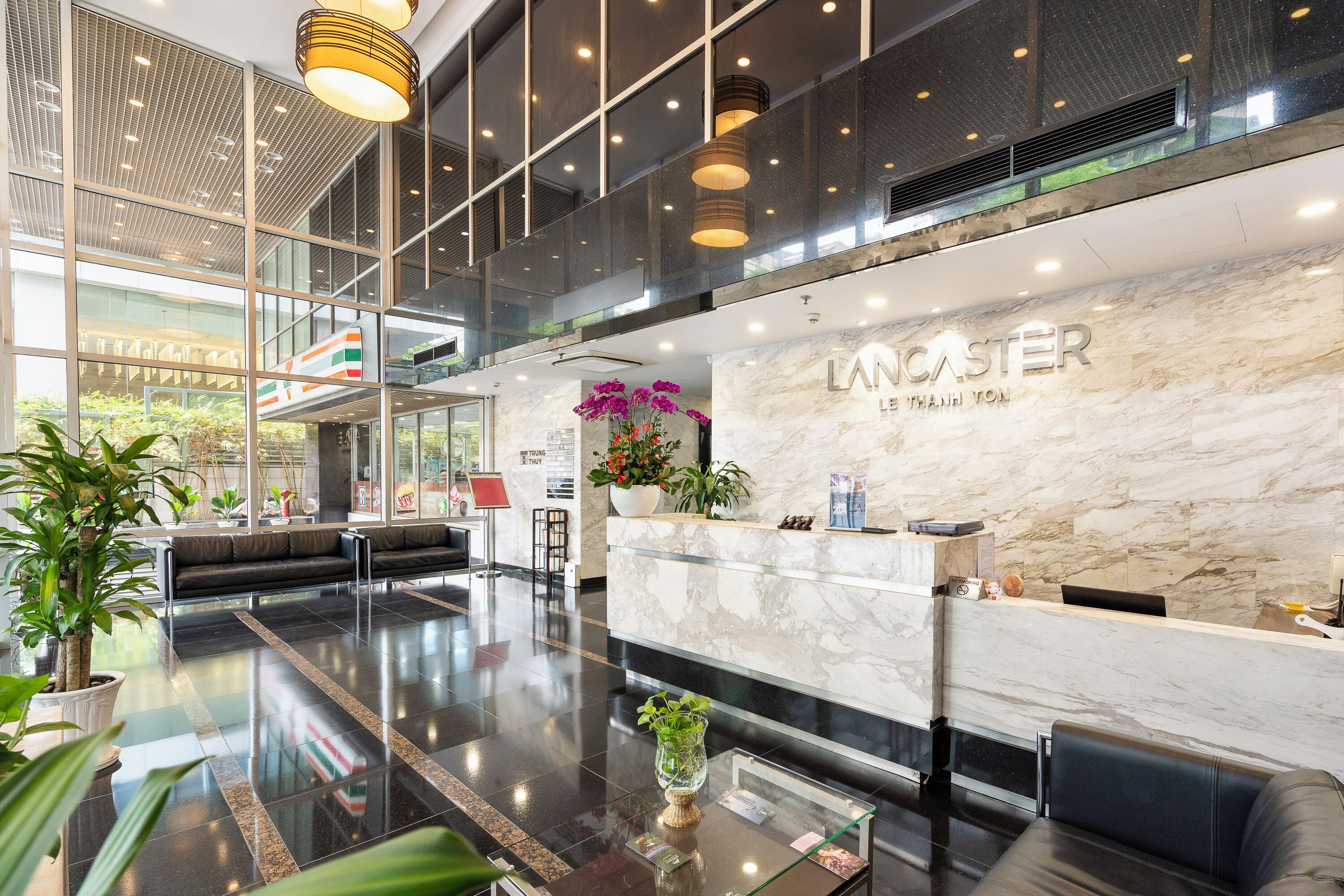 A modern hotel lobby with a reception desk, seating area, and large windows.