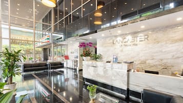 A modern hotel lobby with a reception desk, seating area, and large windows.