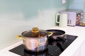 A kitchen with a stove, a pot with a lid, a pan, and a coffee maker. - IMPERIAL JADE SUITES at LANCASTER (Sai Gon)
