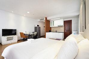 A hotel room with a large bed, a TV, a desk with a chair, a kitchenette, and a bathroom. - IMPERIAL JADE SUITES at LANCASTER (Ho Chi Minh City)