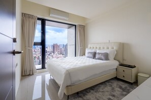 A modern bedroom with a large bed, a nightstand, a small trash bin, and a view of the city through a large window. - 台北中心｜全新景觀豪邸｜高樓層・101城市景觀｜24小時管家保全服務｜全景落地窗與陽台採光 (Taipei City)