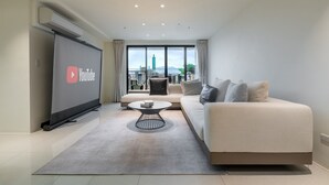 Ett modernt vardagsrum med en stor platt-TV, en soffa, ett soffbord och utsikt över en stadssiluett genom stora fönster.