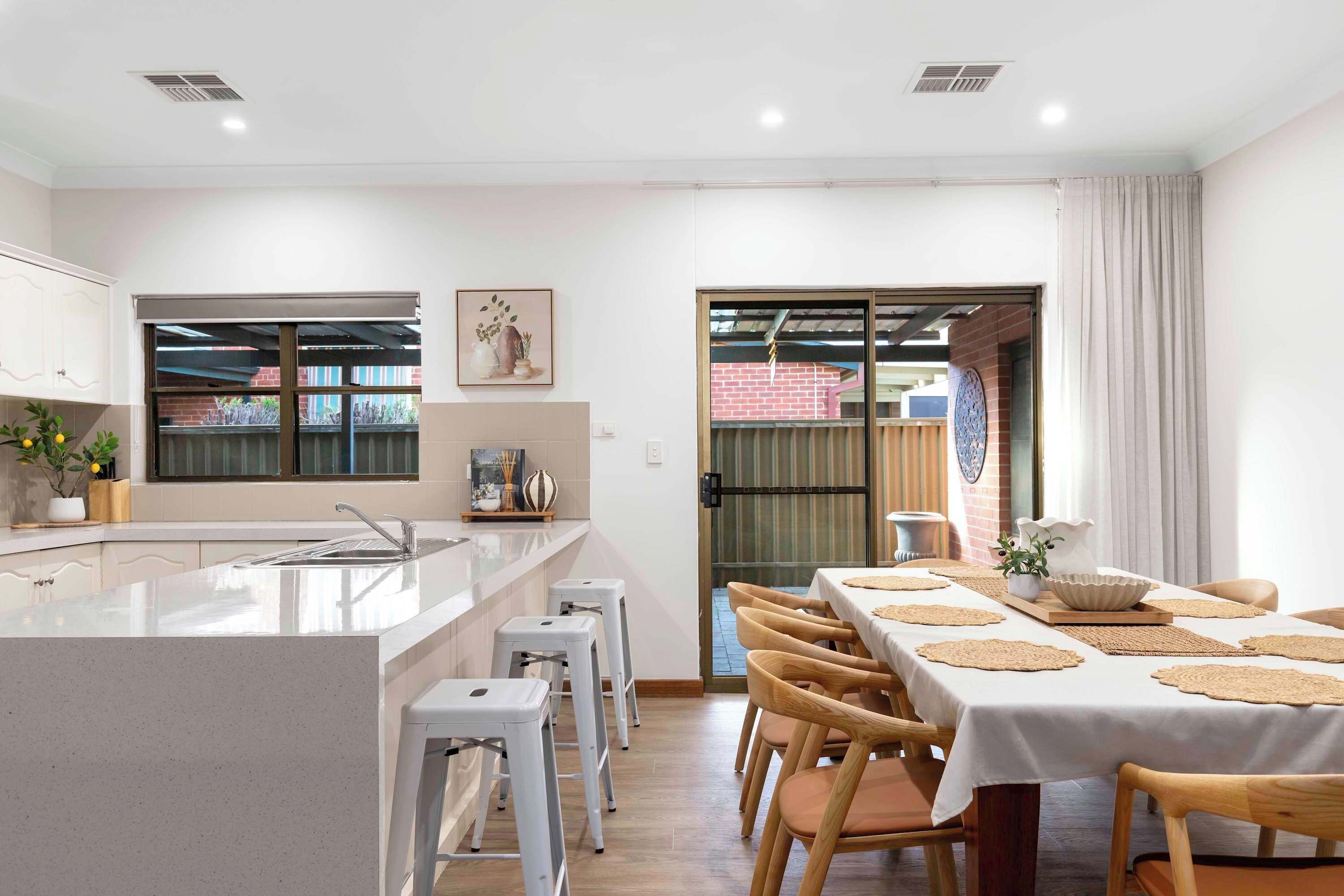 A modern kitchen with a central island, white bar stools, and a dining area with a table set for four.
