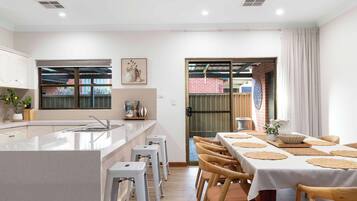 A modern kitchen with a central island, white bar stools, and a dining area with a table set for four.