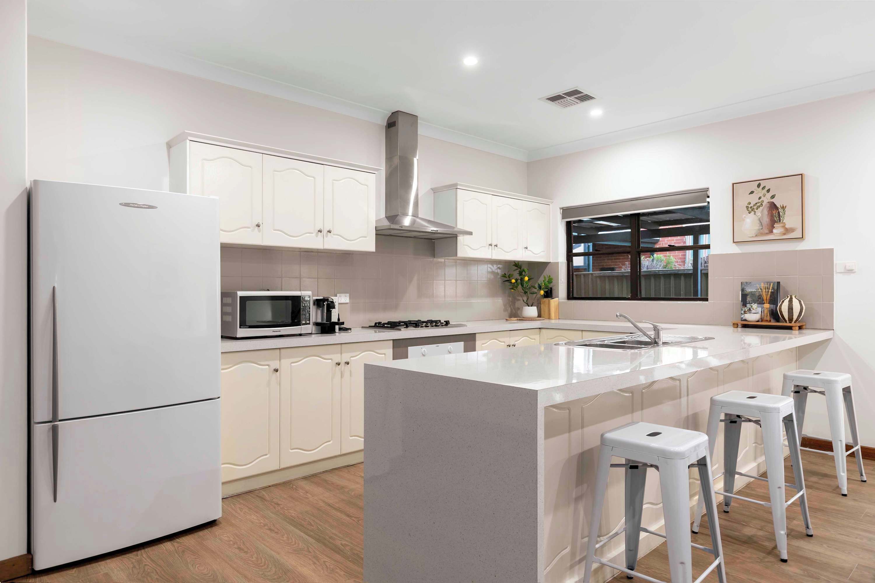 A modern kitchen with white cabinets, a stainless steel range hood, a microwave, a sink, and a window with a view.