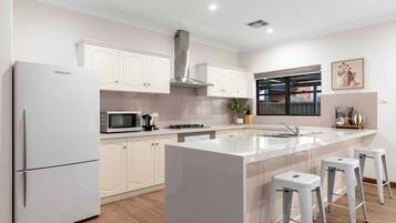 A modern kitchen with white cabinets, a stainless steel range hood, a microwave, a sink, and a window with a view.