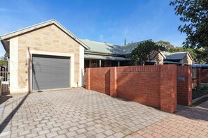 A brick building with a garage, paved driveway, and a brick wall. - Casa Luna | Charming Goodwood Home (Goodwood)