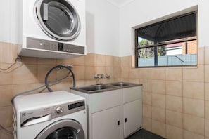 A laundry area with a washing machine, a dryer, and a sink. - Casa Luna | Charming Goodwood Home (Goodwood)