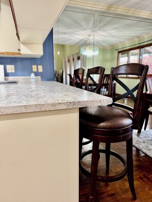 A kitchen area with a marble countertop, wooden chairs, and a view of the dining area. - Charming 3-bedroom rustic bungalow in tranquil Williamsburg sleeps 10 (Williamsburg)