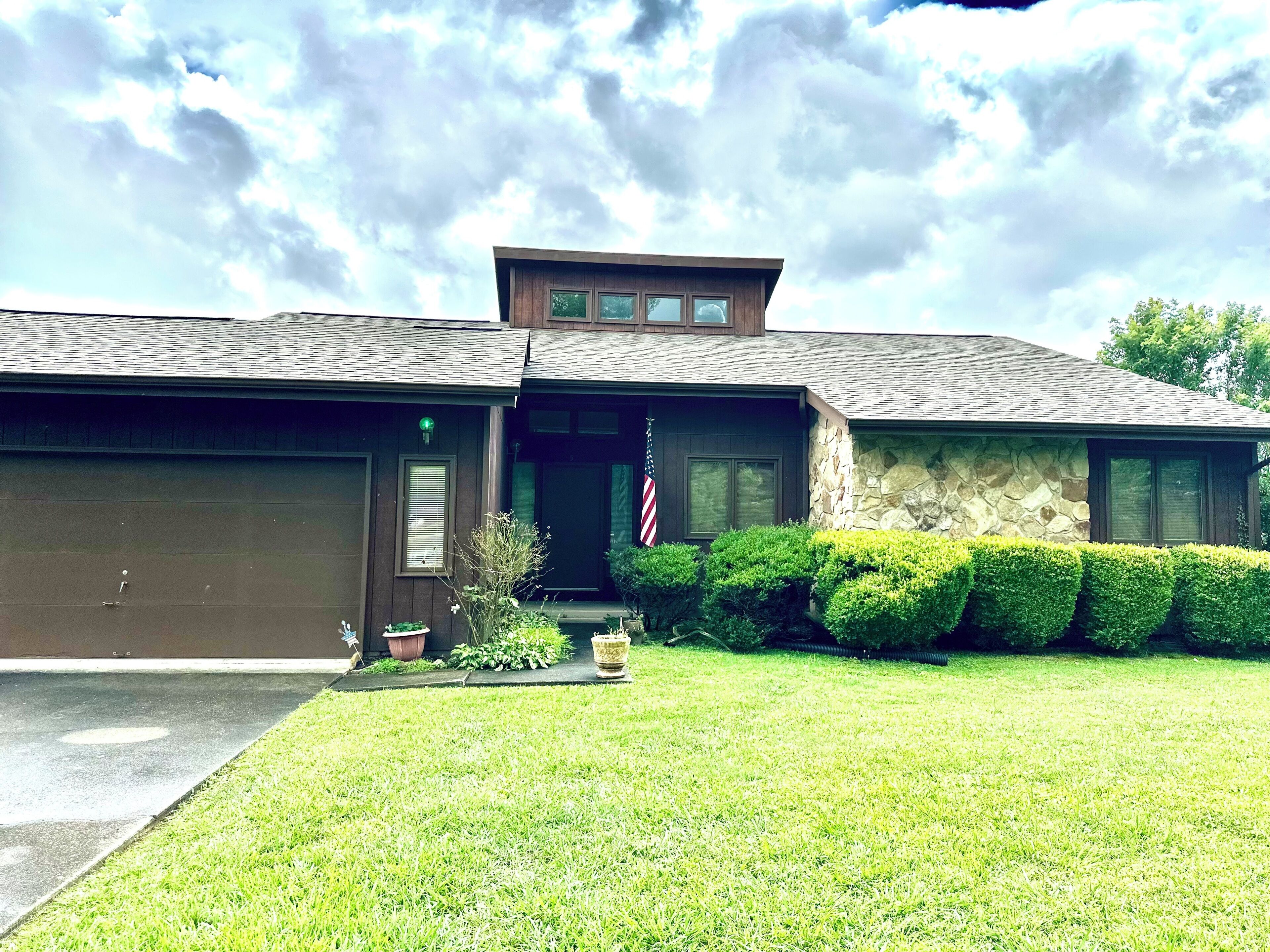 A two-story house with a garage, a stone exterior, and a well-maintained lawn.