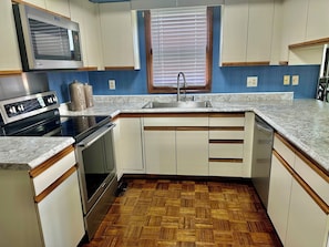 A kitchen with white cabinets, a microwave, a stove, a sink, and a window with blinds. - Charming 3-bedroom rustic bungalow in tranquil Williamsburg sleeps 10 (Williamsburg)