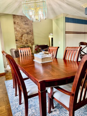 Uma sala de jantar com uma mesa e cadeiras de madeira, um candelabro e uma parede de pedra ao fundo.