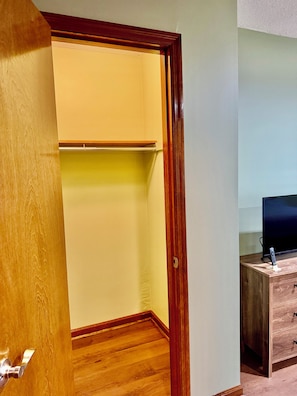 Um quarto com porta e chão de madeira, uma televisão sobre um suporte de madeira, e um controle remoto sobre o suporte.