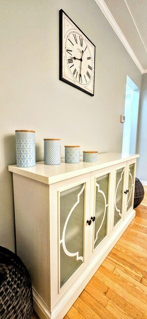 Un armario blanco con puertas de cristal y recipientes decorados encima.
