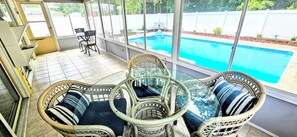 Un patio techado con muebles de mimbre y una mesa de vidrio, con vista a una piscina.