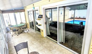 Un patio coperto con una porta vetrata che dà su una piscina, un tavolo con sedie e un cartello che indica un'attesa di 15 minuti.