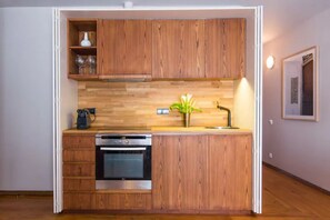 A compact kitchen with wooden cabinetry, a built-in oven, and a small countertop with a coffee maker and a potted plant. - GuestReady - Rivoli Apartment with Balcony (Porto)