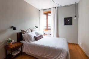 A bedroom with a bed, bedside table, and a window with curtains. - GuestReady - Rivoli Apartment with Balcony (Porto)