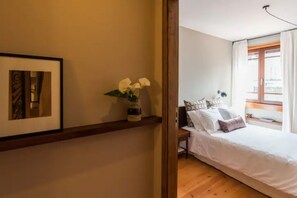 A bedroom with a bed, a nightstand, a vase with flowers, a framed picture on the wall, and a window with curtains. - GuestReady - Rivoli Apartment with Balcony (Porto)