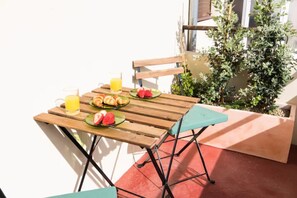 A wooden table with a green chair, a glass of orange juice, and plates with food and watermelon. - GuestReady - Rivoli Apartment with Balcony (Porto)
