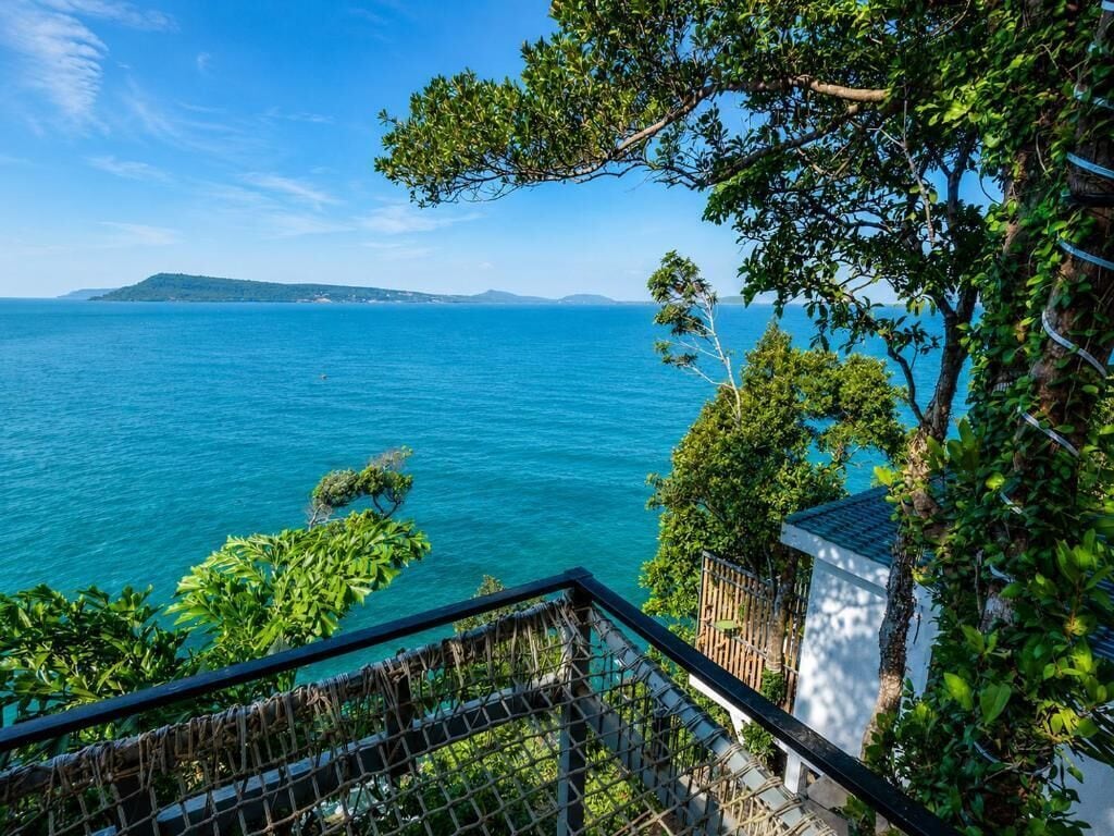 A coastal view with a clear sky, a body of water, and a building with a balcony overlooking the sea.