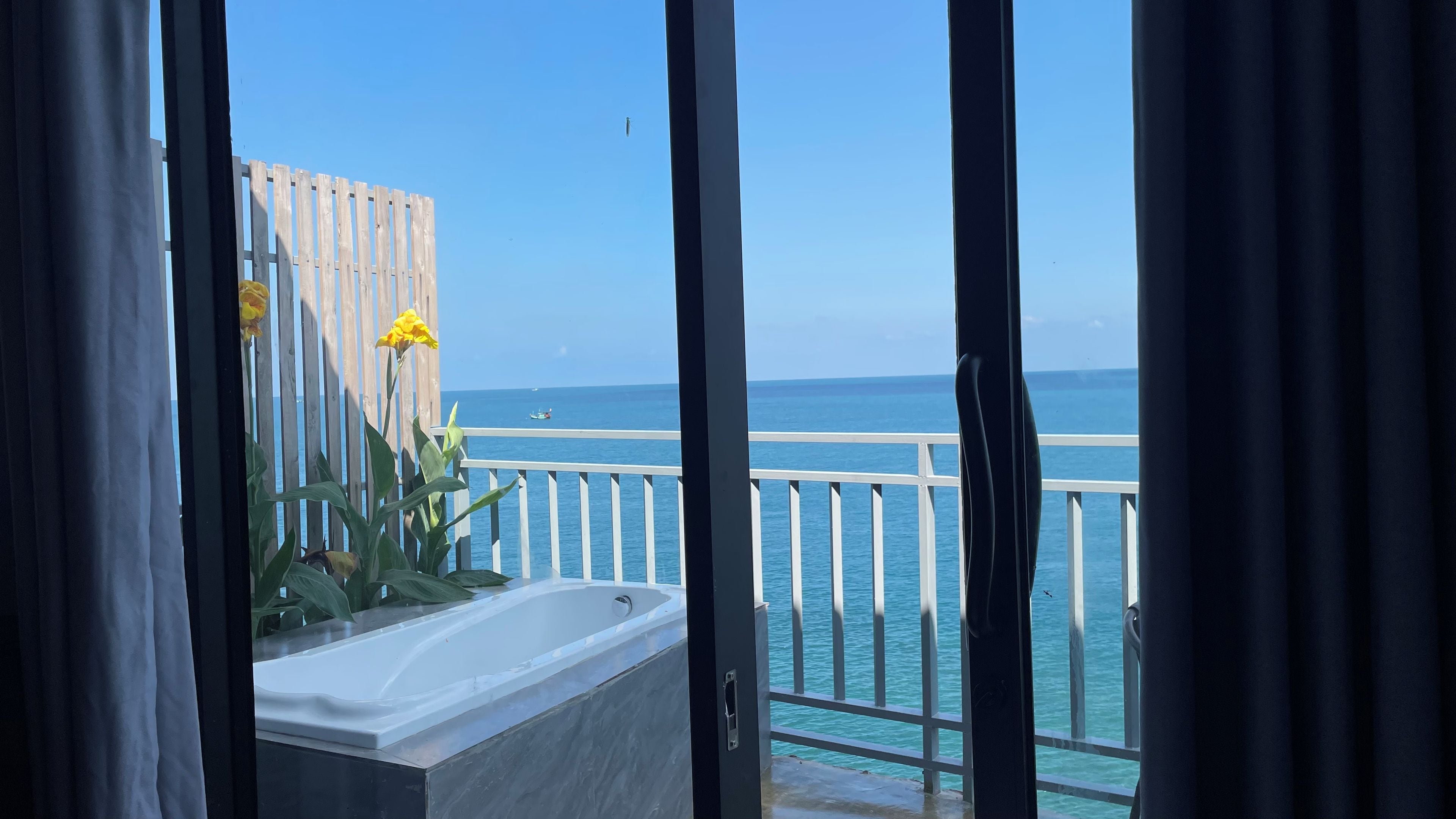 Un balcón con vista al mar, barandilla blanca y una bañera.