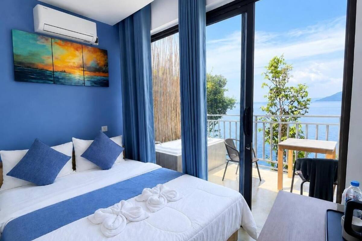 A hotel room with a bed, a painting, a balcony with a table and chairs, and a view of the sea.