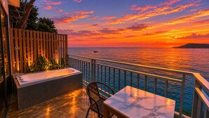 A balcony with a bathtub, a chair, and a table overlooking the sea at sunset. - The Cliff Bungalow (Koh Rong Sanloem)