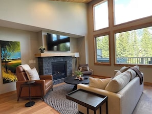 A living room with a fireplace, leather armchair, sofa, coffee table, and large windows.