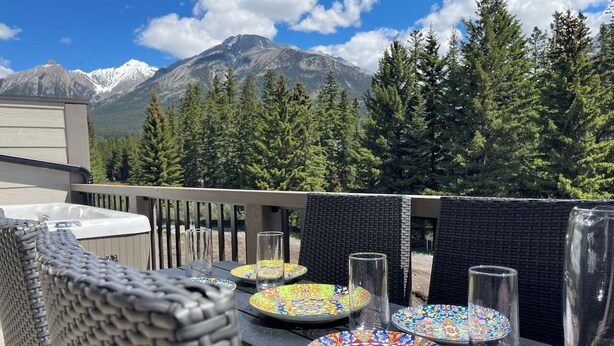 Une terrasse avec des sièges d’extérieur, une table dressée avec des assiettes et des verres, et une vue sur les montagnes en arrière-plan.