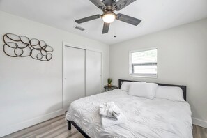Une chambre à coucher avec un lit, un ventilateur de plafond, un élément de décoration murale, une fenêtre et une porte.
