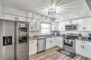 Une cuisine moderne avec des armoires blanches, des appareils en acier inoxydable et un comptoir en granit.