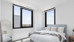 A modern bedroom with a large bed, two windows with black frames, a mirror, and a bedside table. - Family Friendly 3BR Apt with Parking & Workspace (Brunswick)