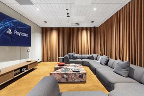 A modern living room with a large flat-screen TV, a sectional sofa, a coffee table, and a wall-mounted sound system. - Parkview 903 | Brunswick 3BR by the Park, Balcony (Brunswick)