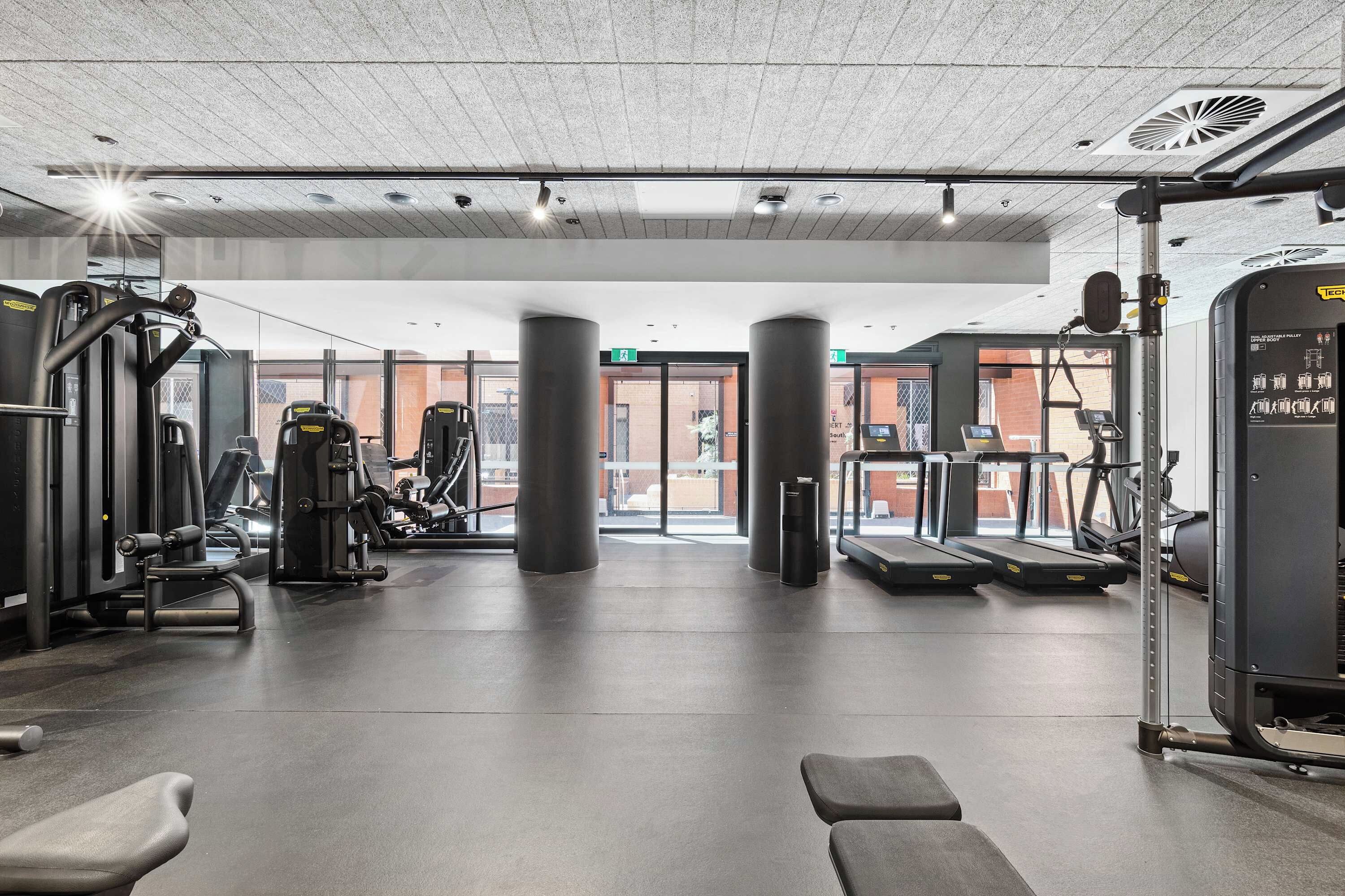 Ein Fitnessraum mit Trainingsgeräten, Laufband und Mülleimer.