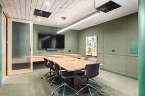 A conference room with a long table, chairs, a flat-screen TV, and a poster on the wall. - Parkview 903 | Brunswick 3BR by the Park, Balcony (Brunswick)